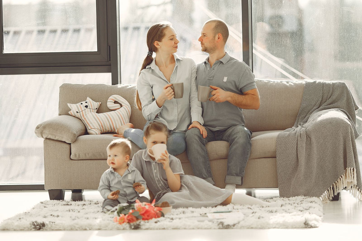 Family relaxing in a bright living room with their baby and toddler on the rug