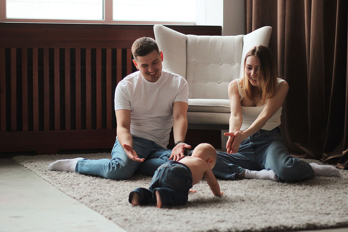 Mum and dad playing with their crawling baby on a living room rug